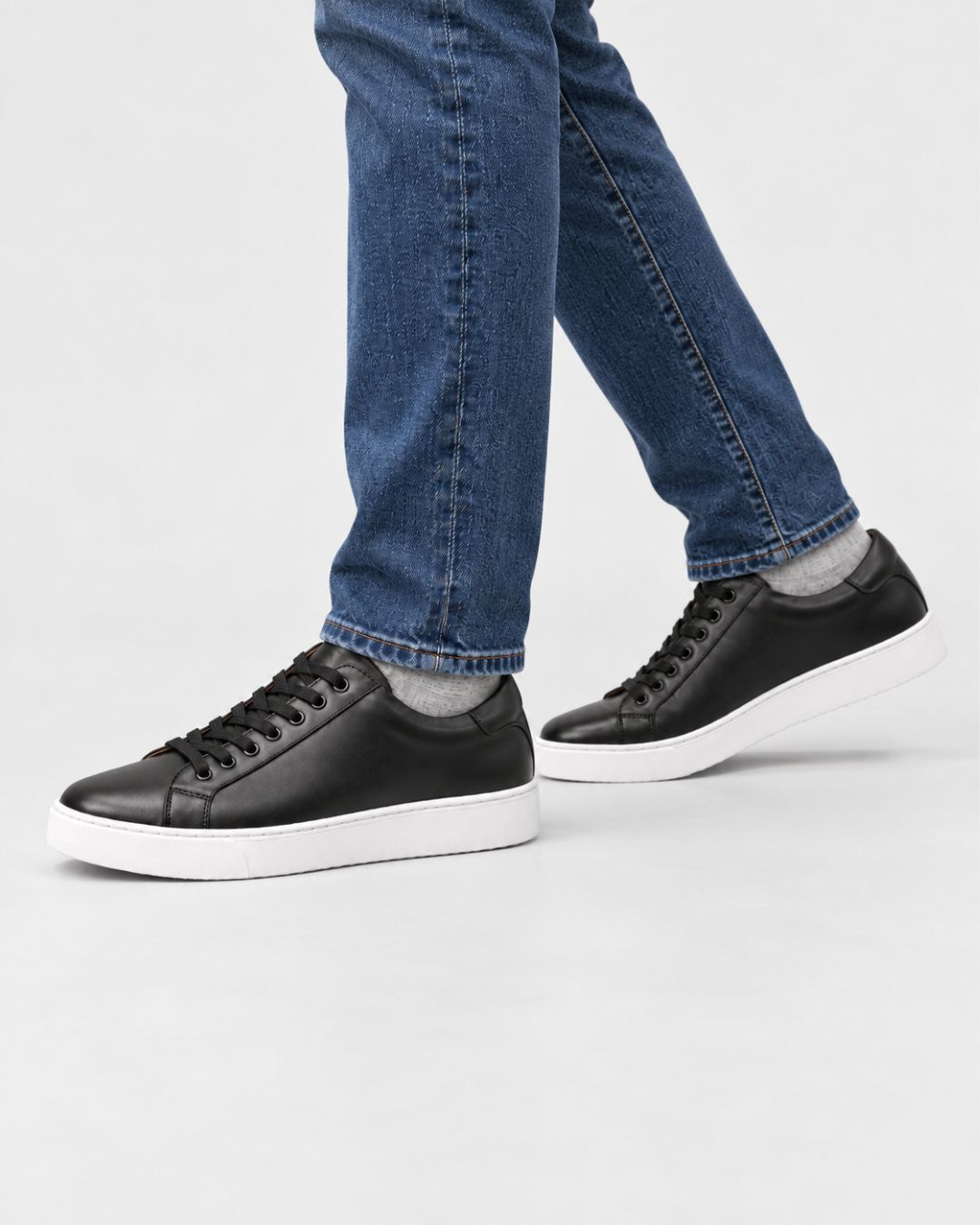 Men's black genuine leather low-top dress sneakers with white rubber soles worn with blue jeans.