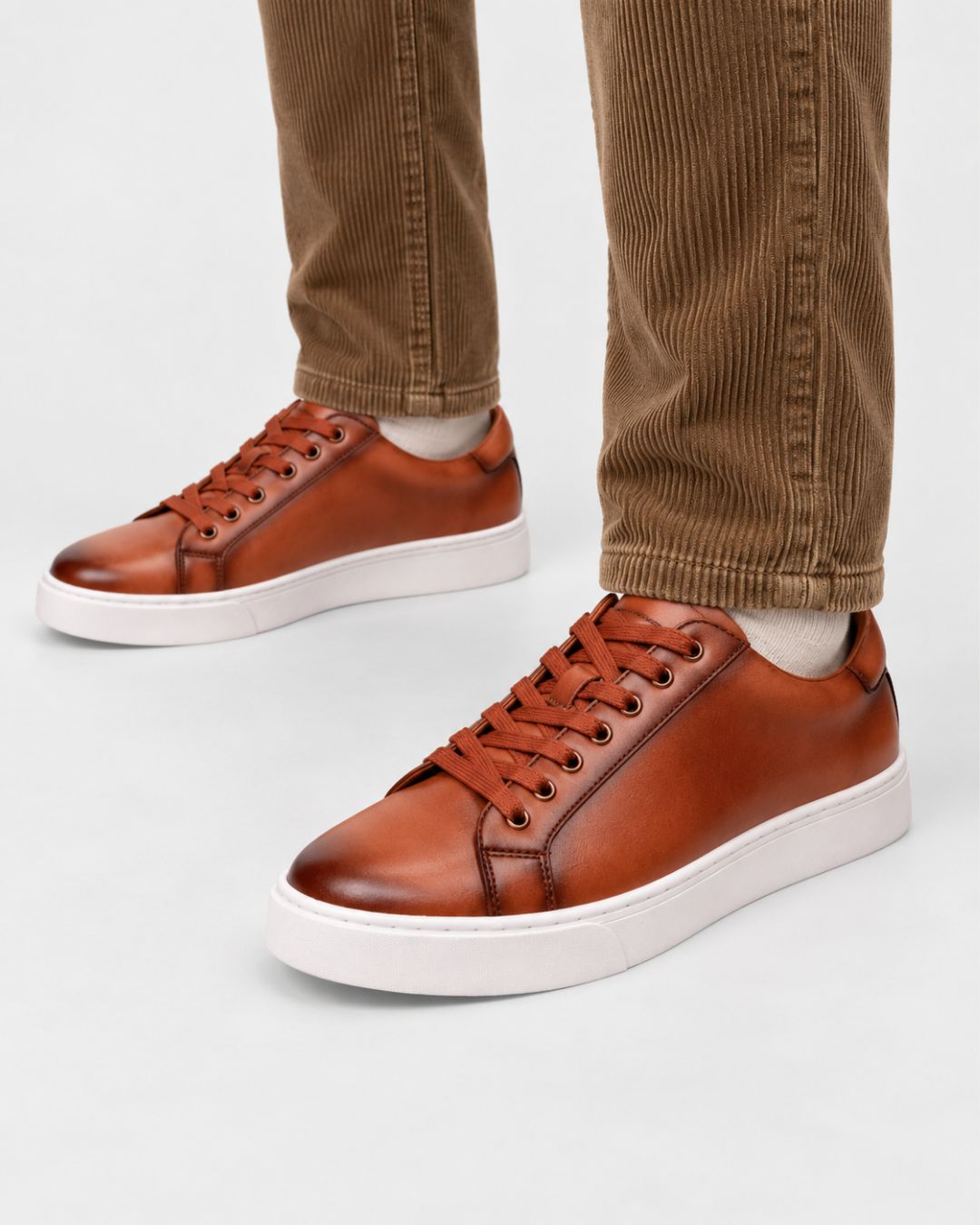 Cognac genuine leather low-top dress sneakers with a white rubber sole and matching laces worn with brown corduroy trousers.