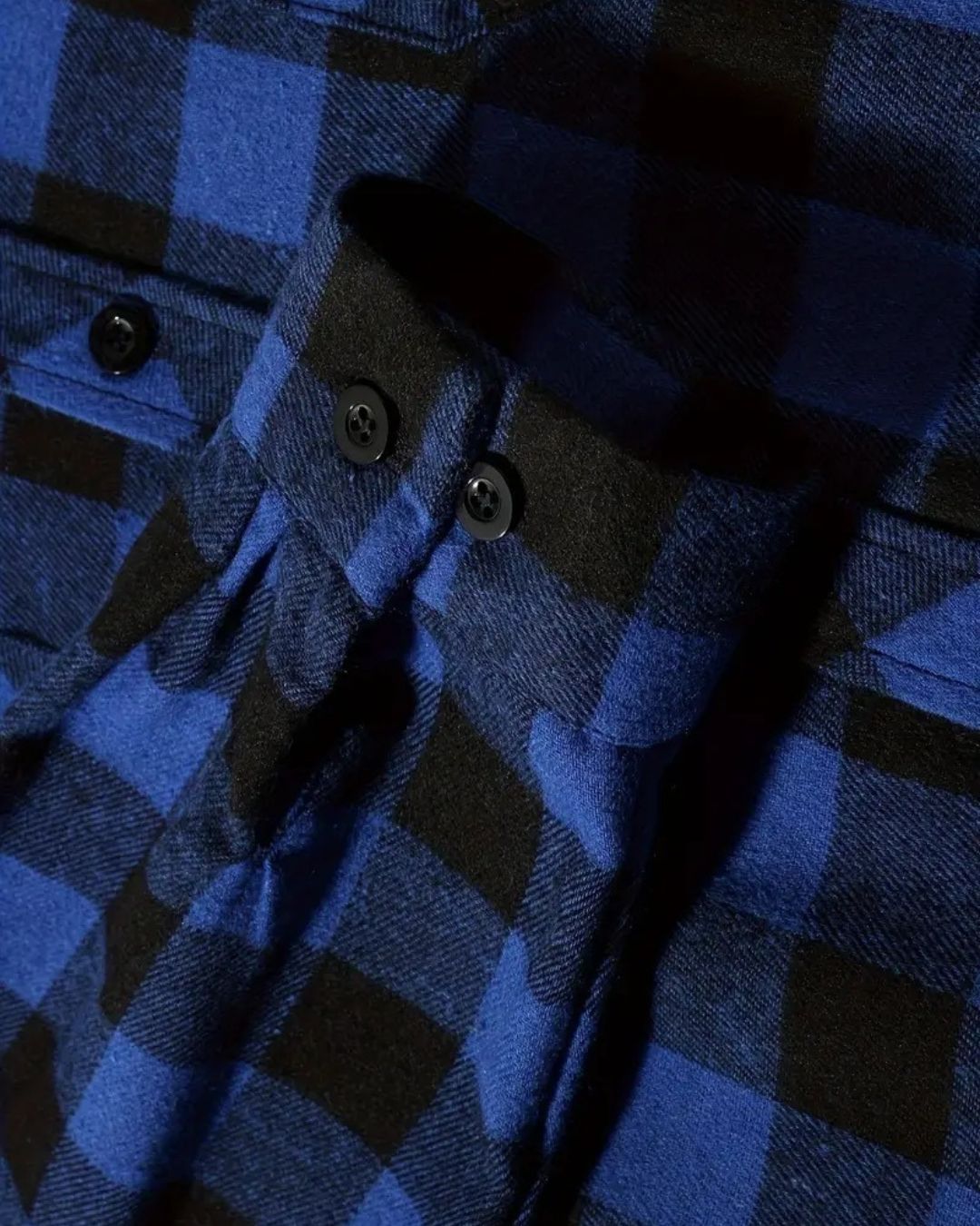 Close-up of a soft, blue and black plaid brushed flannel shirt featuring buttoned cuffs and chest pockets.