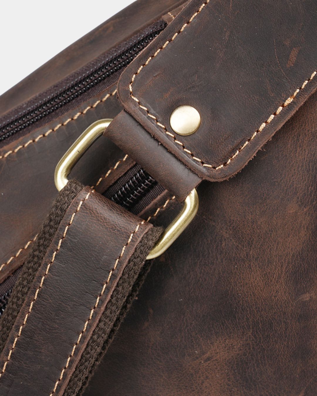Close-up of a brown vintage leather crossbody sling bag featuring reinforced stitching, a brass buckle, and a secure zip.