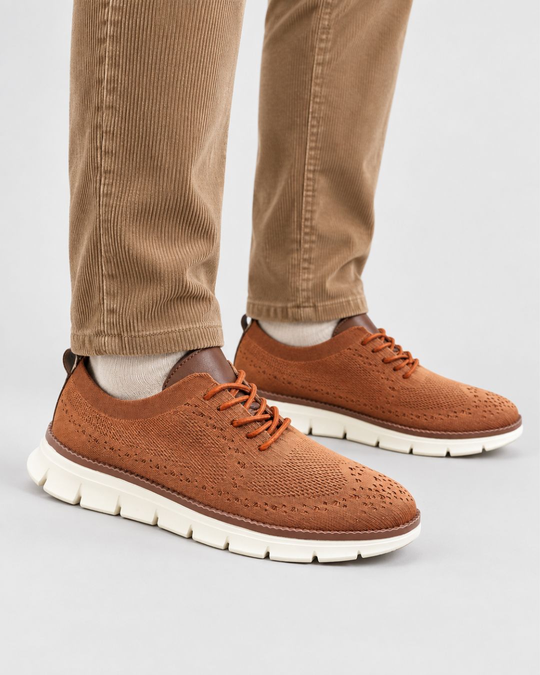 Men’s tan breathable mesh dress sneakers with lace-up closure and a cushioned white EVA sole, worn with corduroy trousers.