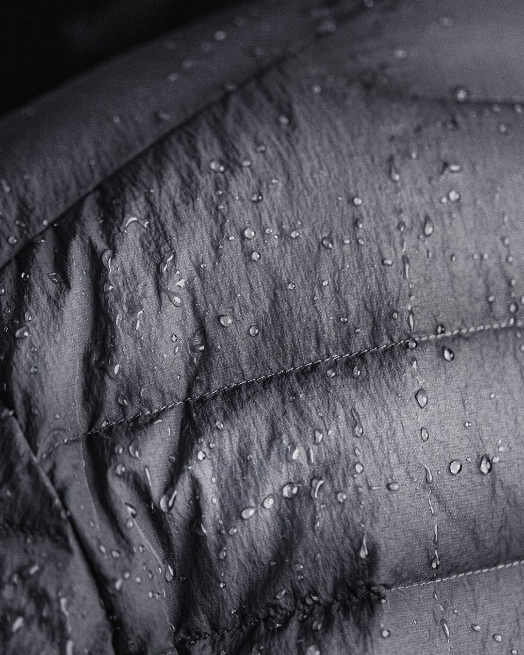 Close-up of a black, quilted duck down puffer jacket featuring a water-repellent finish with visible water droplets.