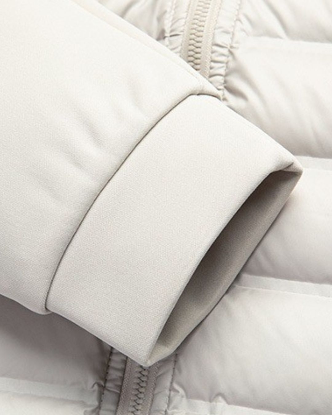 Close-up of a beige hybrid puffer jacket featuring a quilted down body and a smooth, ribbed knit sleeve cuff.