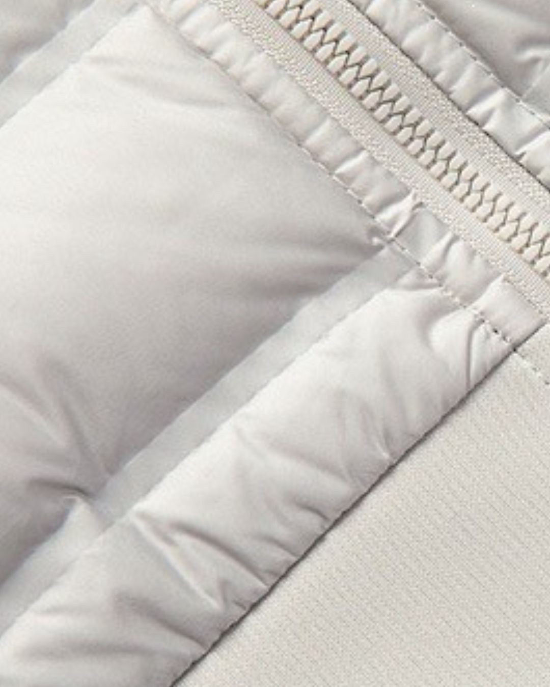 Close-up of a light grey hybrid puffer jacket featuring quilted down-filled panels, a sturdy zipper, and soft knit fabric.