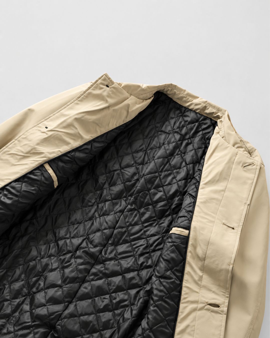 Beige men’s short trench coat featuring a black quilted lining and a clean, button-front car coat silhouette.