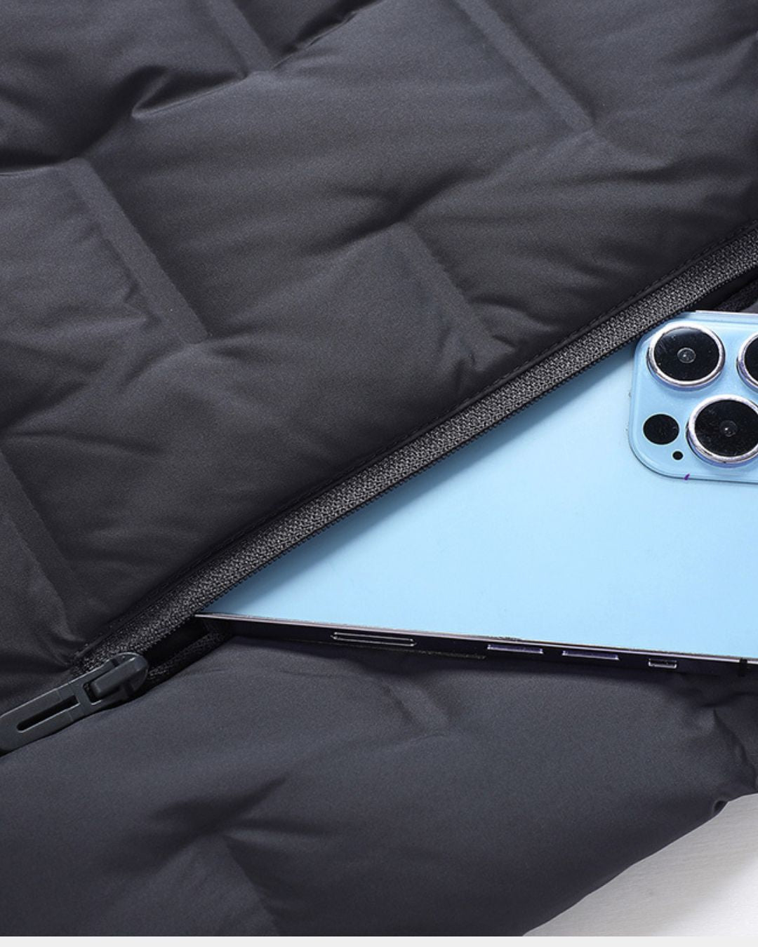 Close-up of a black quilted down puffer jacket featuring a zippered pocket holding a light blue smartphone.