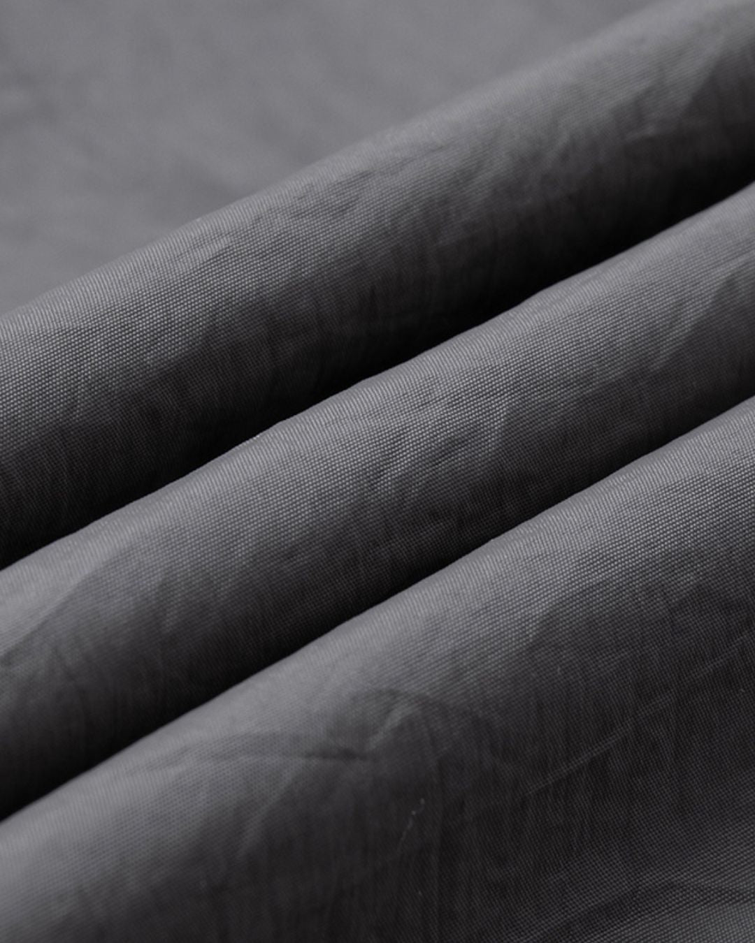 Close-up of charcoal grey waterproof nylon fabric with a fine-weave texture for a lightweight windbreaker jacket.