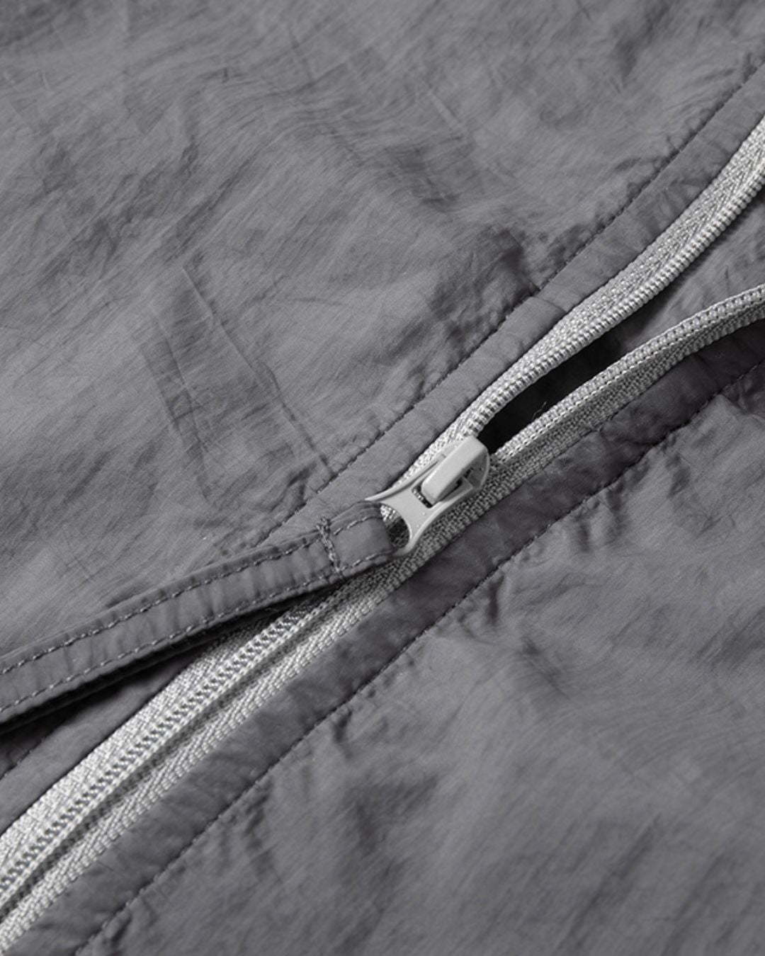 Close-up of a grey, lightweight, waterproof nylon windbreaker featuring a durable zipper and textured fabric finish.