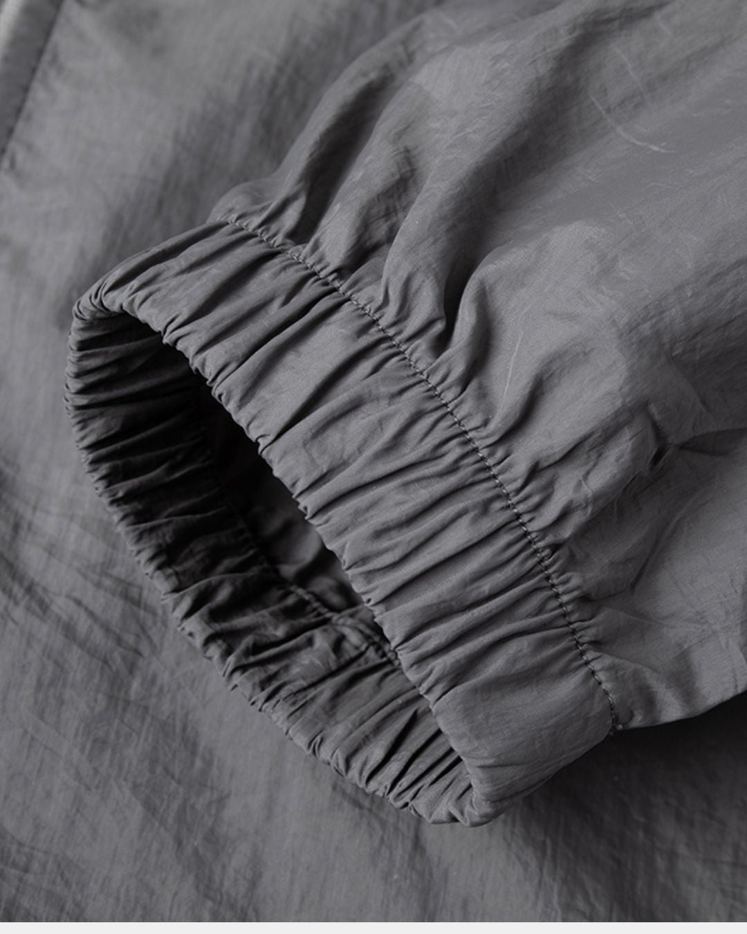 Close-up of a charcoal grey men's windbreaker sleeve featuring a comfortable, elasticized gathered cuff.