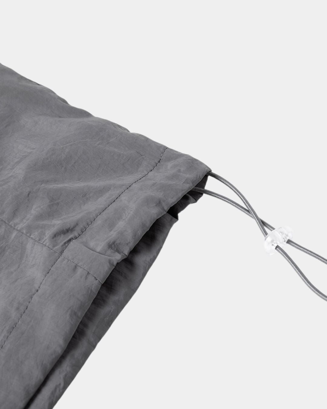 Close-up of a charcoal grey nylon windbreaker featuring an adjustable drawstring hem with a clear plastic toggle.