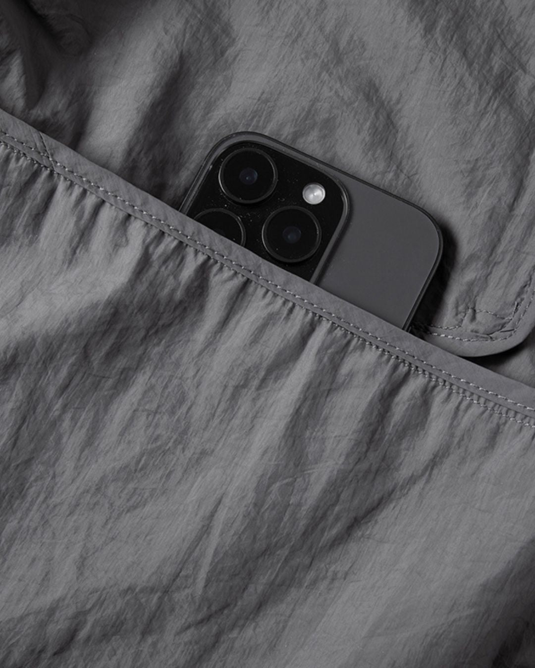 Smartphone tucked into the zippered chest pocket of a grey, lightweight, waterproof nylon windbreaker jacket.
