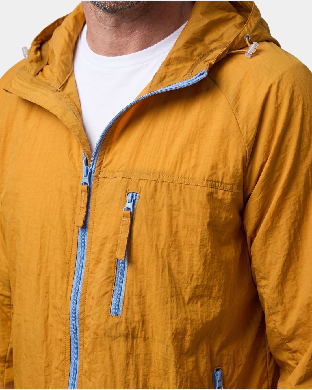 Mustard yellow lightweight hooded windbreaker with light blue zippers and a zippered chest pocket on a man.