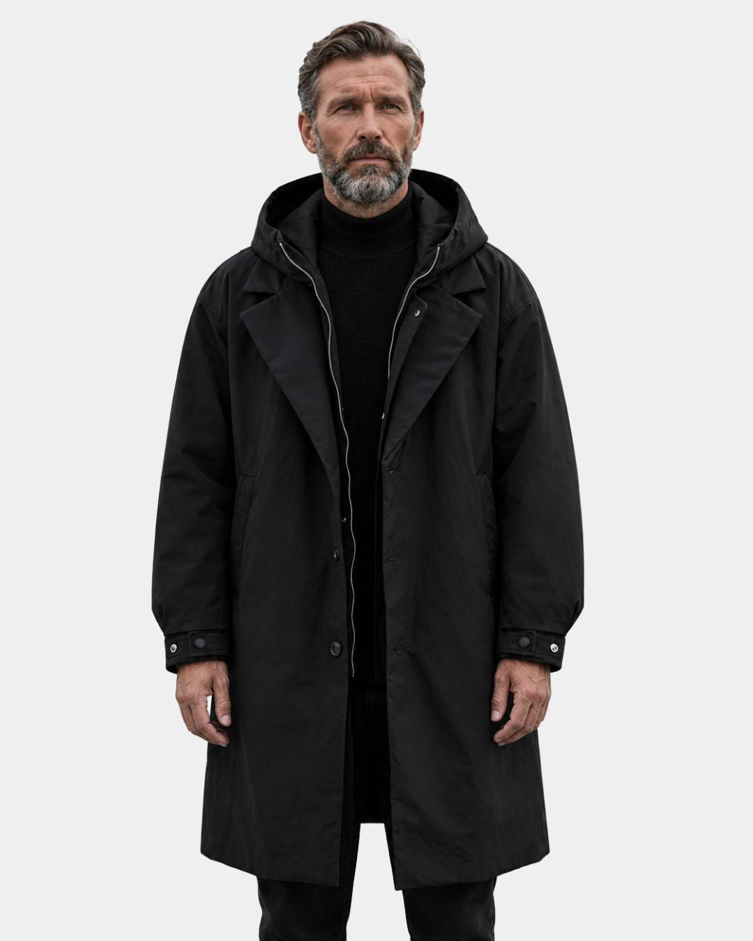 Man wearing a black long hooded overcoat with a zip and button front, trench-inspired collar, and adjustable cuffs.