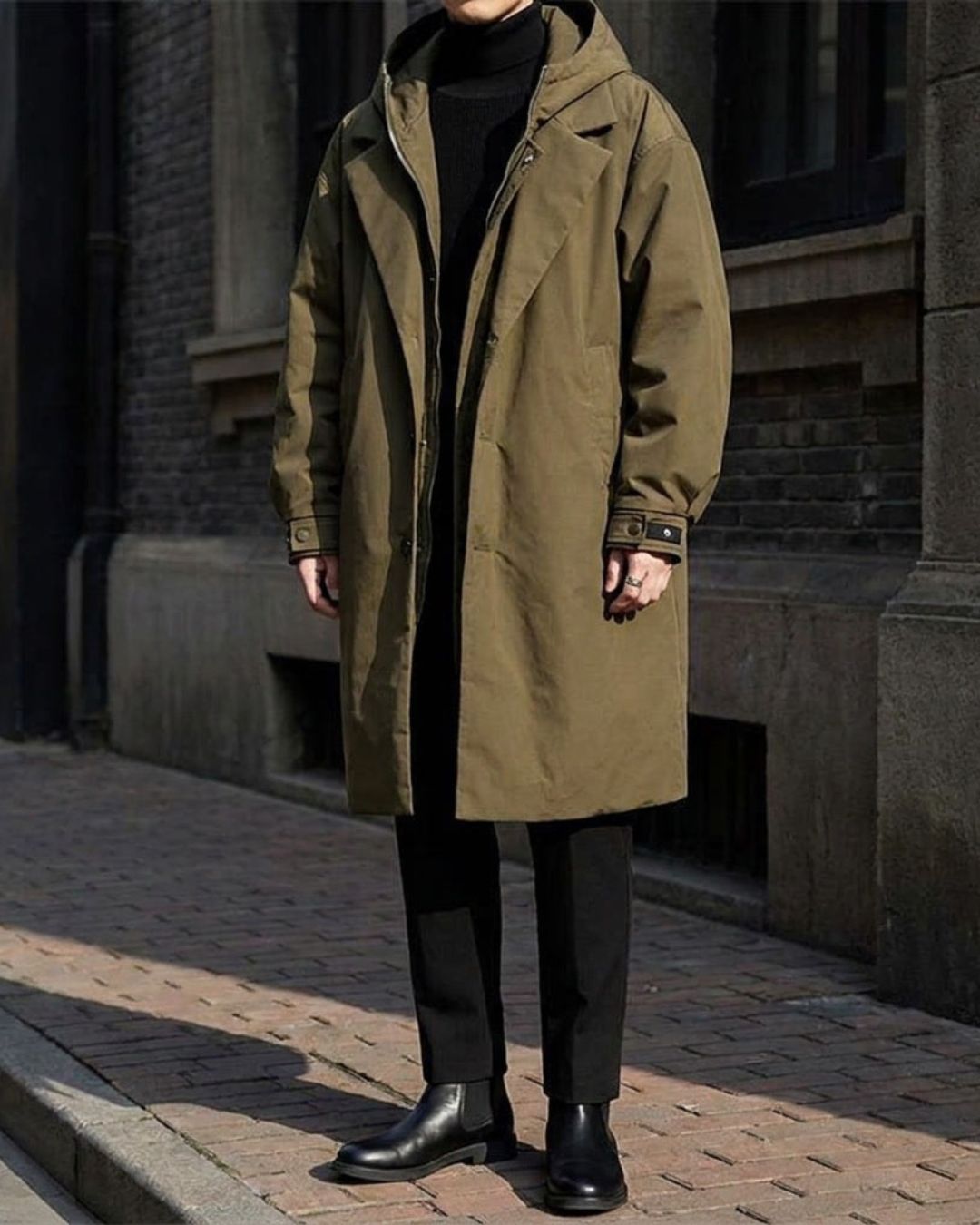 Olive green men’s long hooded overcoat with a trench-inspired design, full zip, and button closure for a refined urban look.
