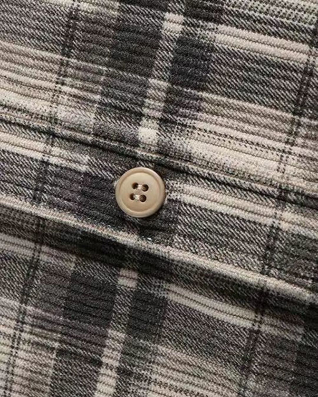 Close-up of a grey and beige plaid corduroy shirt featuring a textured ribbed fabric and a single button closure.