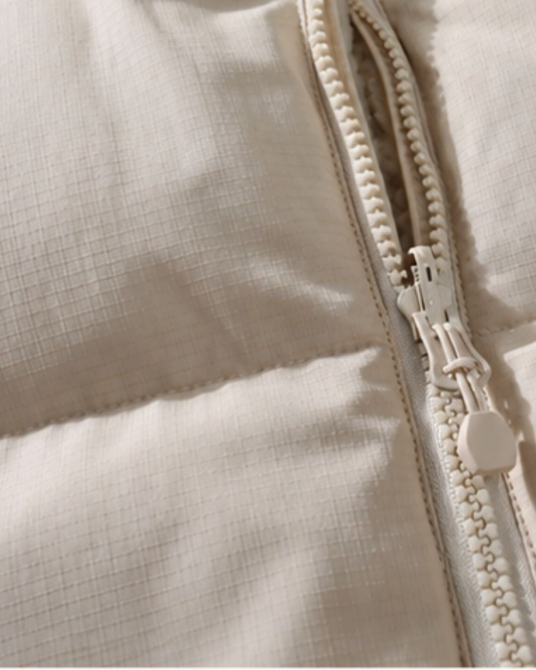 Close-up of a beige reversible puffer jacket featuring a textured padded shell and a sturdy matching front zipper.
