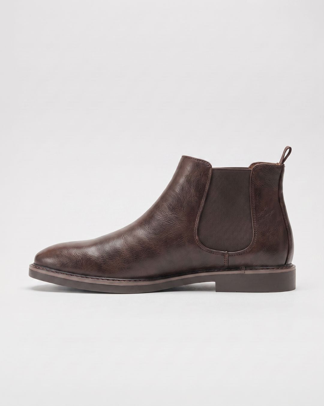 A dark brown leather Chelsea boot shown in a side profile view against a light gray studio background.