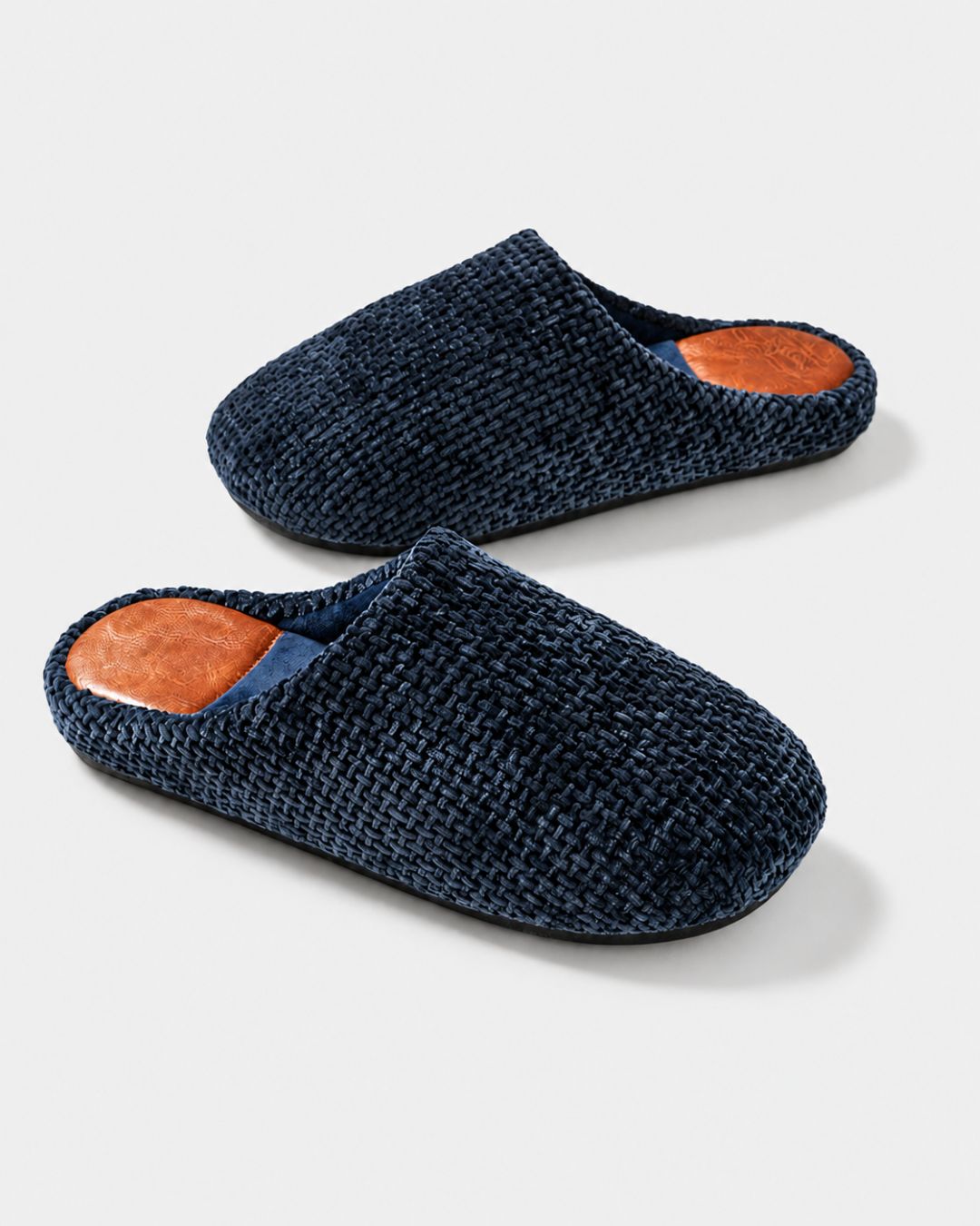 Men’s navy blue woven suede house slippers with a plush lining and tan leather-look heel inserts on a white background.