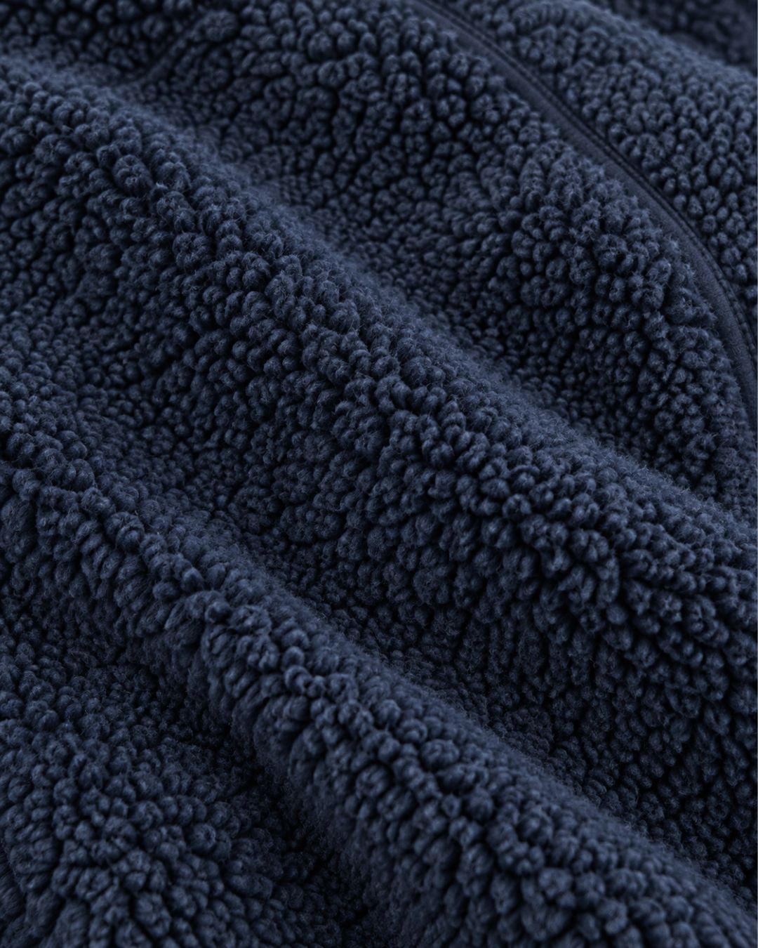 Close-up of a navy blue men’s teddy sherpa fleece jacket showing the soft, textured material and a full-zip closure.