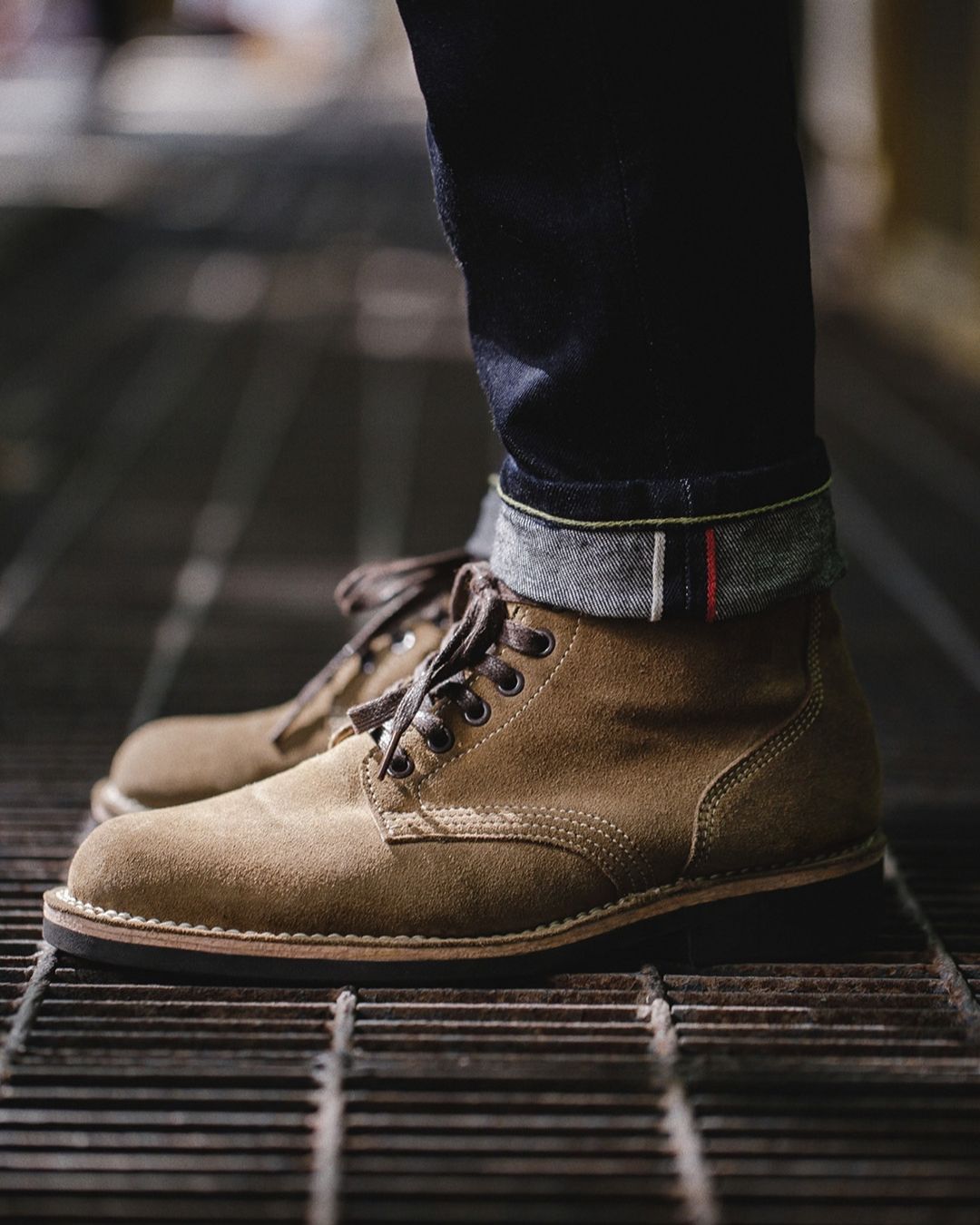 Men’s tan suede lace-up ankle boots with contrast stitching, round toe, and durable rubber outsole worn with cuffed denim.