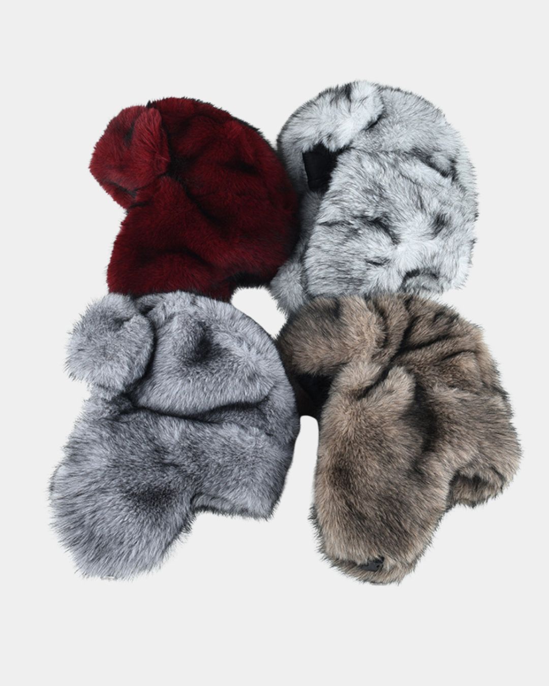 Four plush ushanka trapper hats in red, white, grey, and brown, featuring soft ear flaps for winter warmth.
