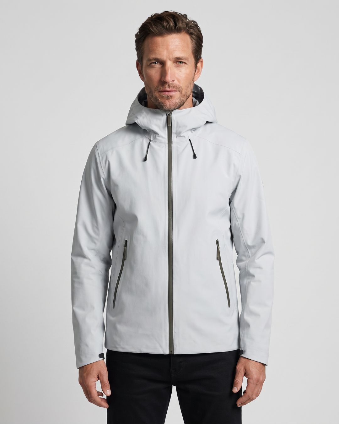Man wearing a light grey waterproof hooded hiking windbreaker with a full-zip front and zippered pockets.