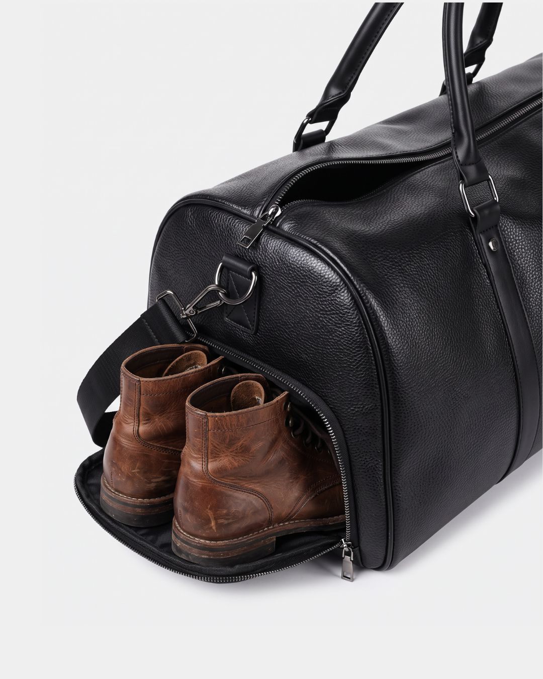 Black textured leather weekender duffel bag with a dedicated side shoe compartment containing brown leather boots.