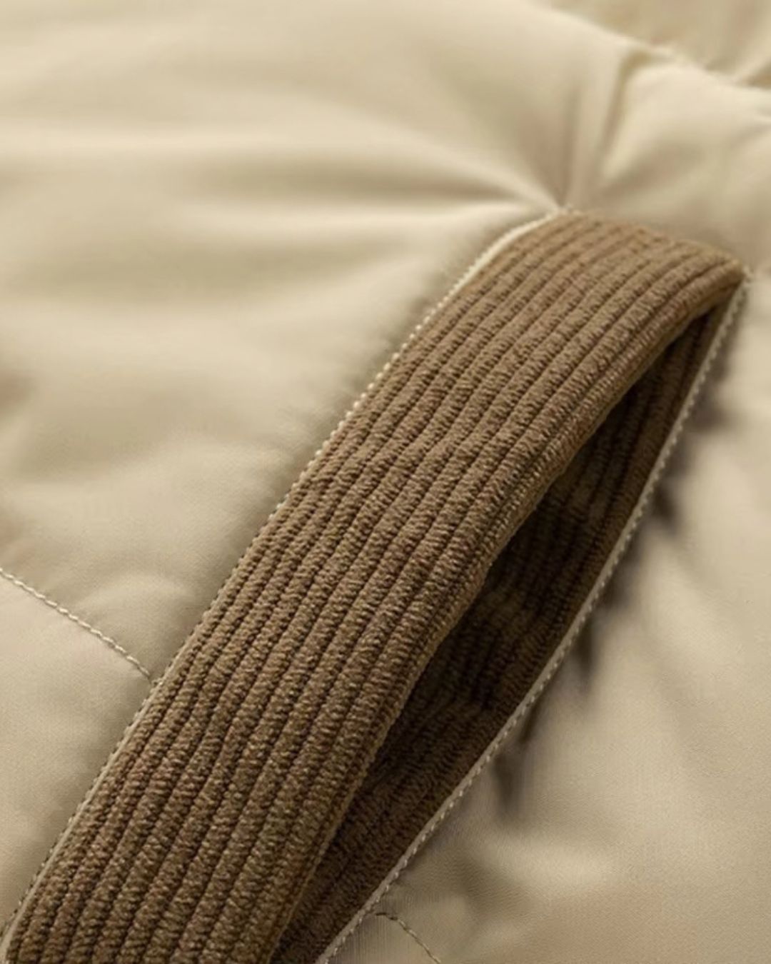 Beige puffer jacket pocket featuring brown corduroy trim detail on a padded, insulated winter coat.