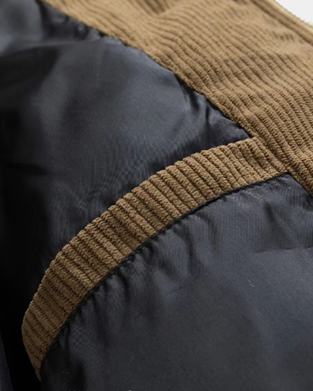 Close-up of a black puffer jacket featuring brown corduroy trim detailing on the shoulder and fabric seams.