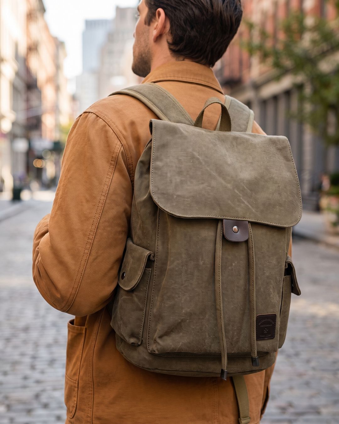 A man viewed from behind carrying a large khaki canvas backpack on his back, by Hudson & Tate.