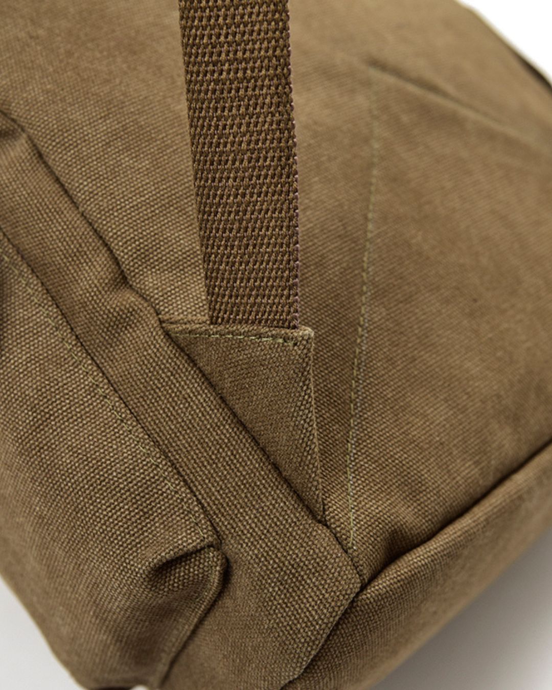 Close-up detail of a khaki canvas bag showing the fabric texture, stitching, and a vertical webbed strap.