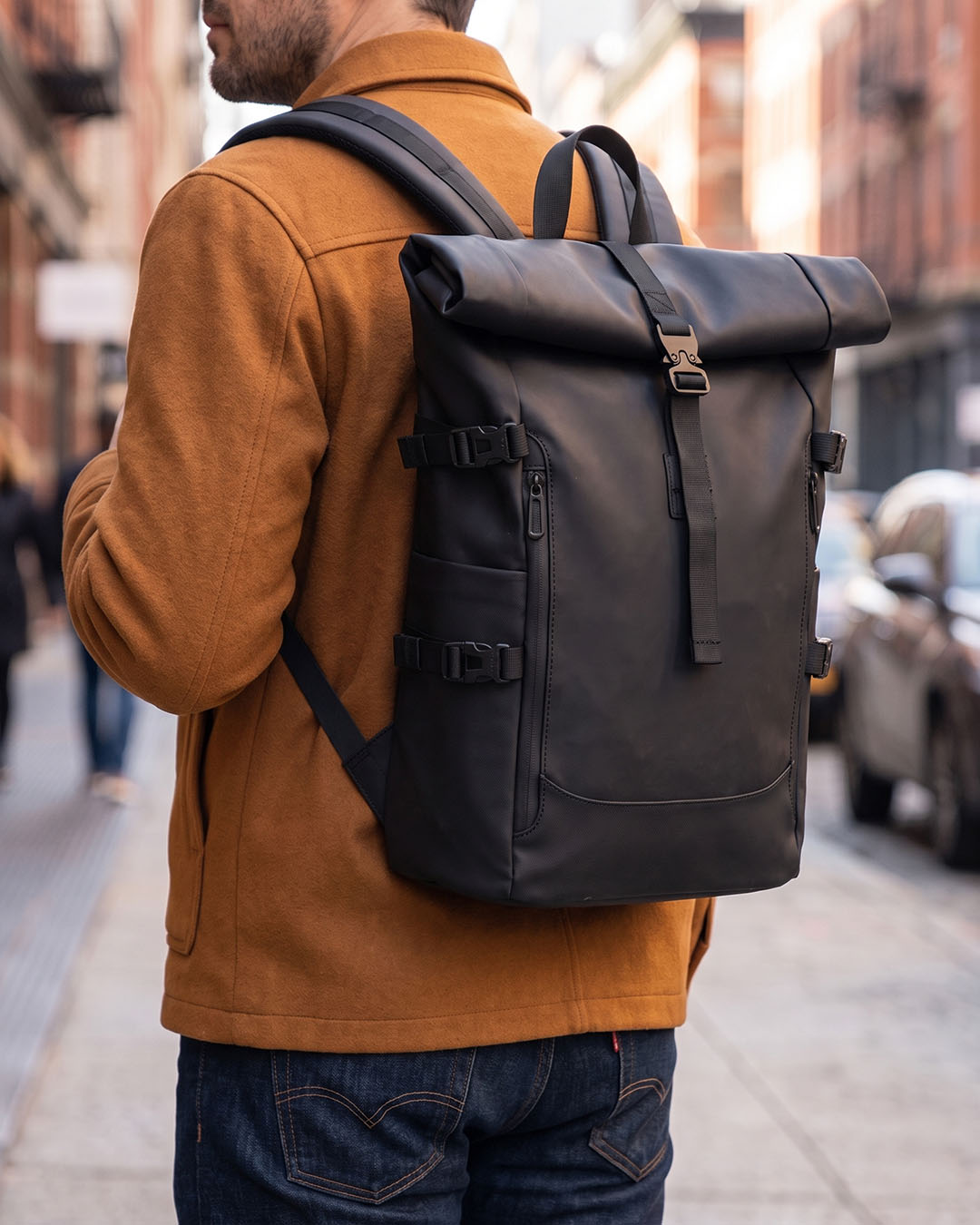 A man carrying the black tucker waterproof laptop travel backpack by Hudson & Tate on a city street.