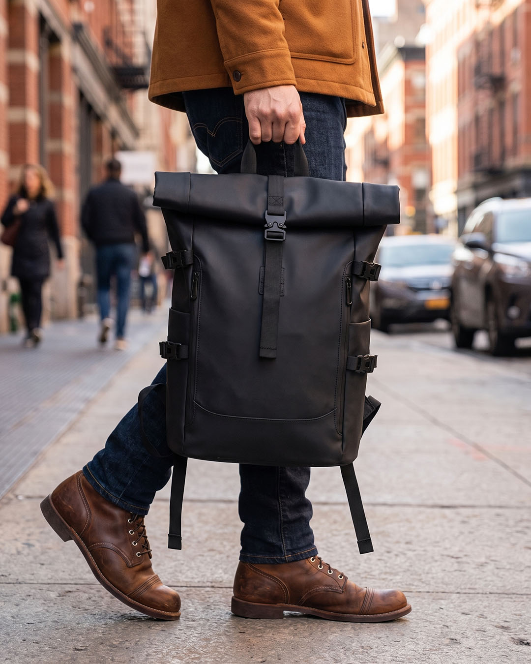 A man carrying the black tucker waterproof laptop travel backpack by Hudson & Tate on a city street.